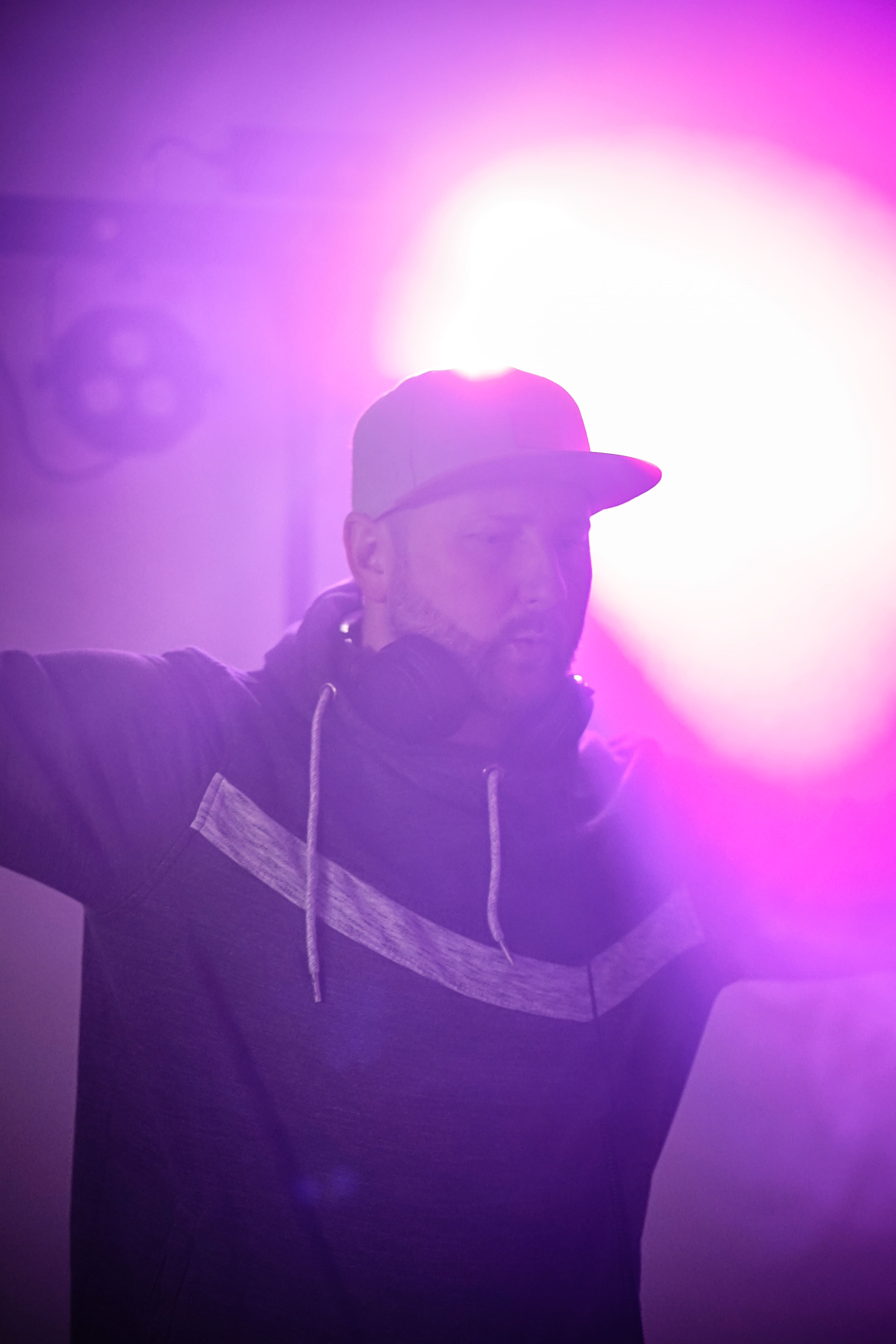 DJ Tony Lötzke mit Cap und Kopfhörern unter intensivem violettem Bühnenlicht und Nebeleffekten bei einem Event